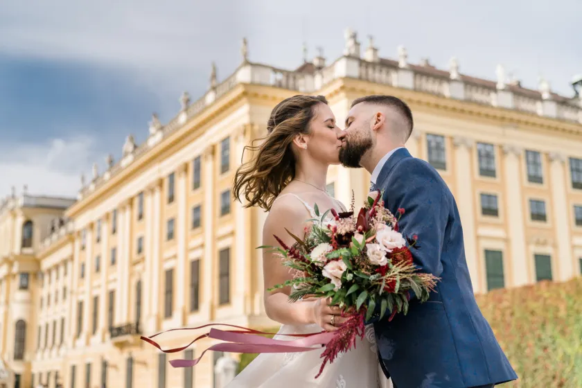 The bride and groom kiss in front of Schönbrunn Palace after their dream wedding.